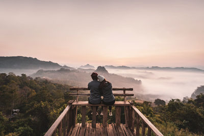 People looking at mountain against sky during sunset