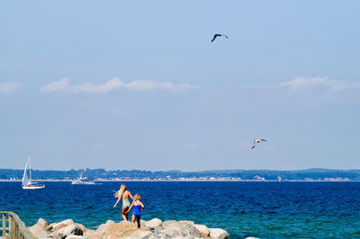 Rear view of women walking on rocks at sea shore against sky