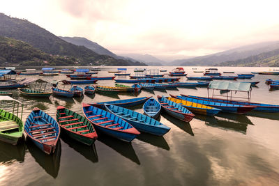 Multi colored boats moored in lake against sky during sunset