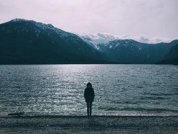 Rear view of silhouette person on lake against mountains