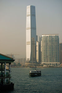 Sailboats in sea against modern buildings in city against sky