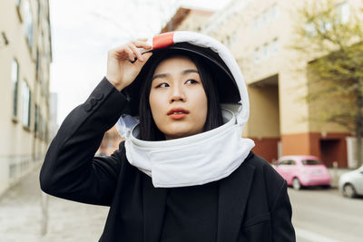 Beautiful woman looking away while holding space helmet in city