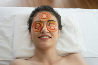 Young woman with tomato slices on eyes lying in spa
