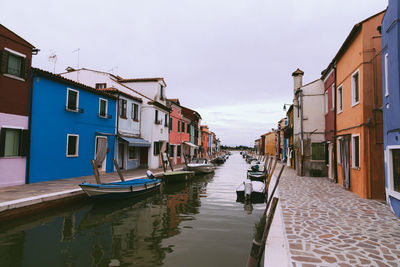 Boats moored in canal amidst buildings in city against sky