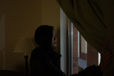 Side view of woman looking through window at home