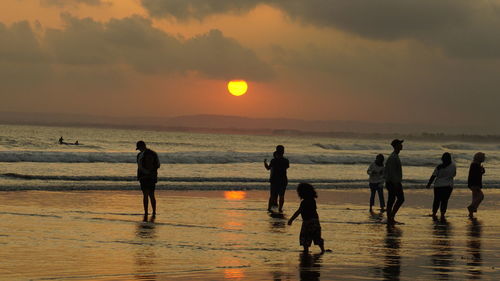 Silhouette people on beach against sky during sunset