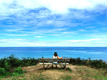 Rear view of girl sitting on bench by sea