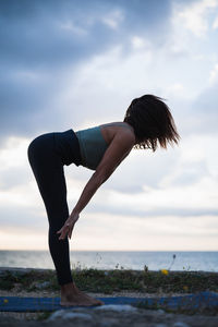 Side view of woman performing yoga exercises in a natural setting with cloudy skies.