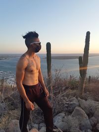 Young man standing on beach against sky during sunset