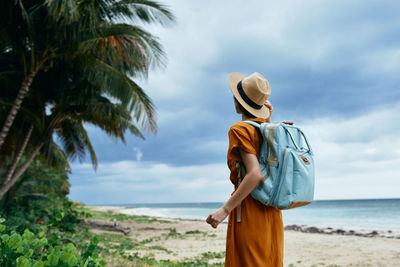 Rear view of woman standing at beach against sky