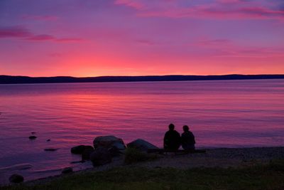 Silhouette people sitting on beach against sky during sunset