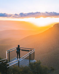 Man standing on railing against sky during sunset