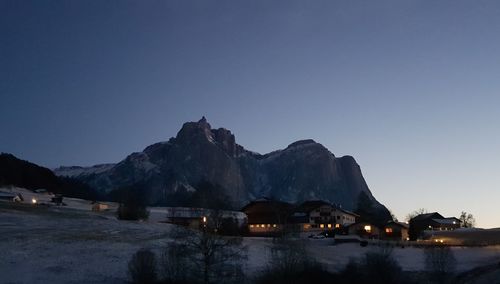 Illuminated buildings by mountains against clear blue sky