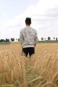 Rear view of man standing on field against cloudy sky