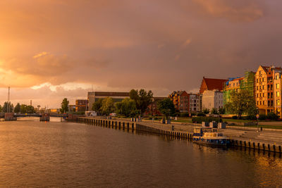 Bridge over river by buildings against sky during sunset