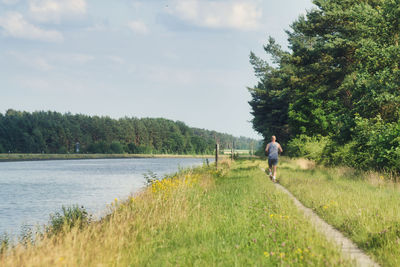 Man running on grassy field by canal against sky