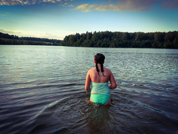 Rear view of woman standing in lake against sky