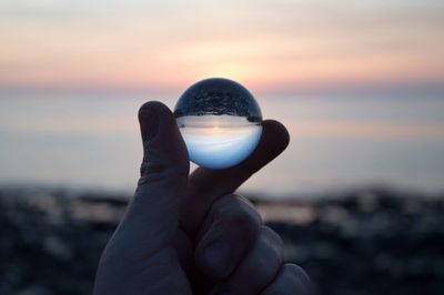 Cropped hand holding crystal ball with reflection at sunset