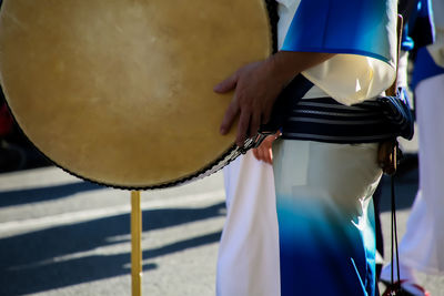 Midsection of person holding drum while standing on footpath 