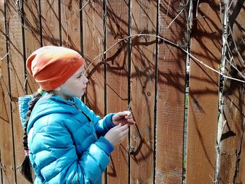 Cute girl looking away while standing by fence during winter