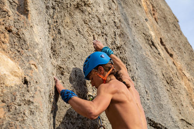 Shirtless man wearing helmet rock climbing