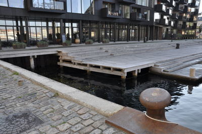 Empty bench by footpath against buildings in city
