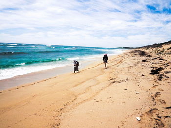 Man and woman walking on shore against cloudy sky