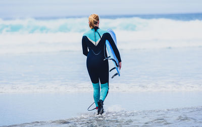 Rear view of woman with surfboard walking at beach