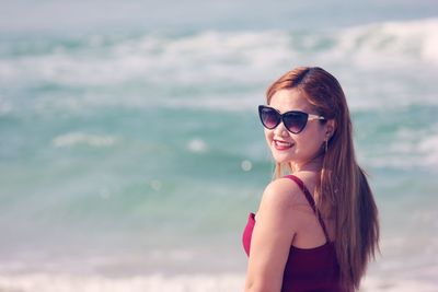 Portrait of young woman wearing sunglasses standing at beach