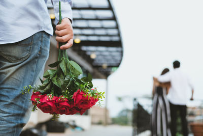 Midsection of man holding rose bouquet while couple standing against clear sky