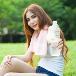 Portrait of woman holding water bottle while sitting on field