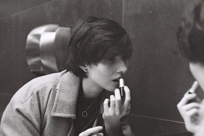 Young woman applying lipstick in front of mirror