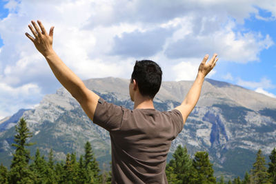 Rear view of man with arms raised against mountains