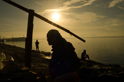 Silhouette people fishing on beach against sky during sunset