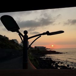 Silhouette street light on beach against sky during sunset