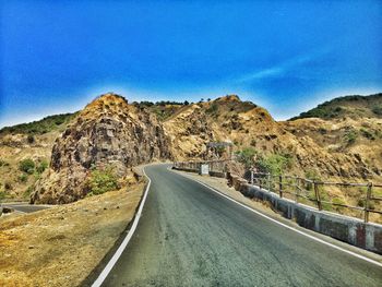 Empty road by mountain against blue sky