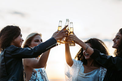 Happy friends holding beer bottle against sky