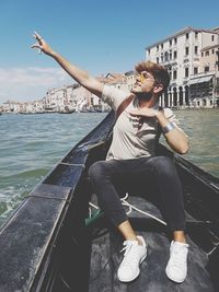 Man sitting by water in city against sky