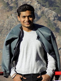 Portrait of young man standing at observation point against mountain