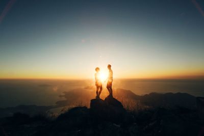 Silhouette couple standing on rock formation against sky during sunset