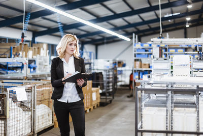 Blond businesswoman standing in shop floor, writing in notebook