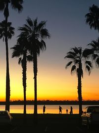 Silhouette people amidst palm trees at beach against orange sky