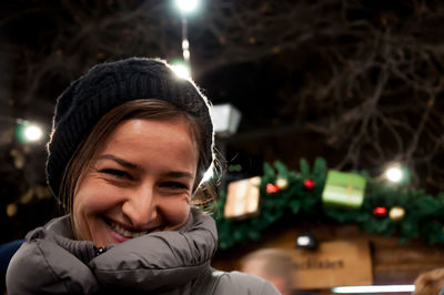 Portrait of smiling young woman in illuminated christmas tree during winter