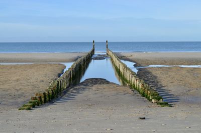 Wooden posts in sea against sky