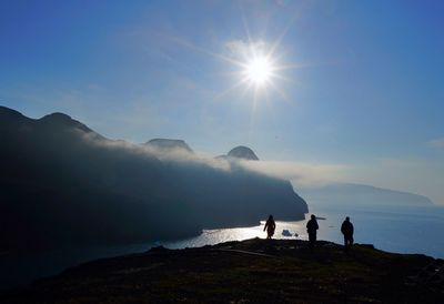 People standing on shore by sea against sky during sunset