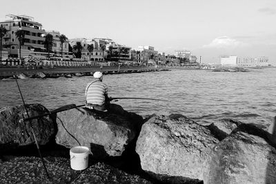 Rear view of woman by sea against sky in city