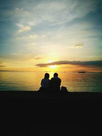 Silhouette couple sitting on beach against sky during sunset