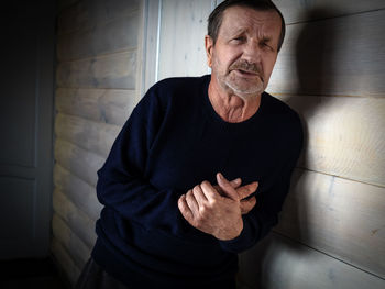 Portrait of man with chest pain by wall at home