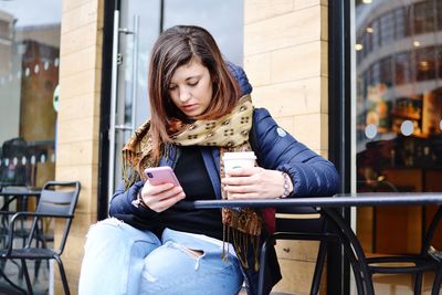 Full length of young woman using phone while sitting in cafe