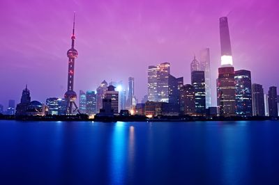 Illuminated skyscrapers in city by huangpu river against sky